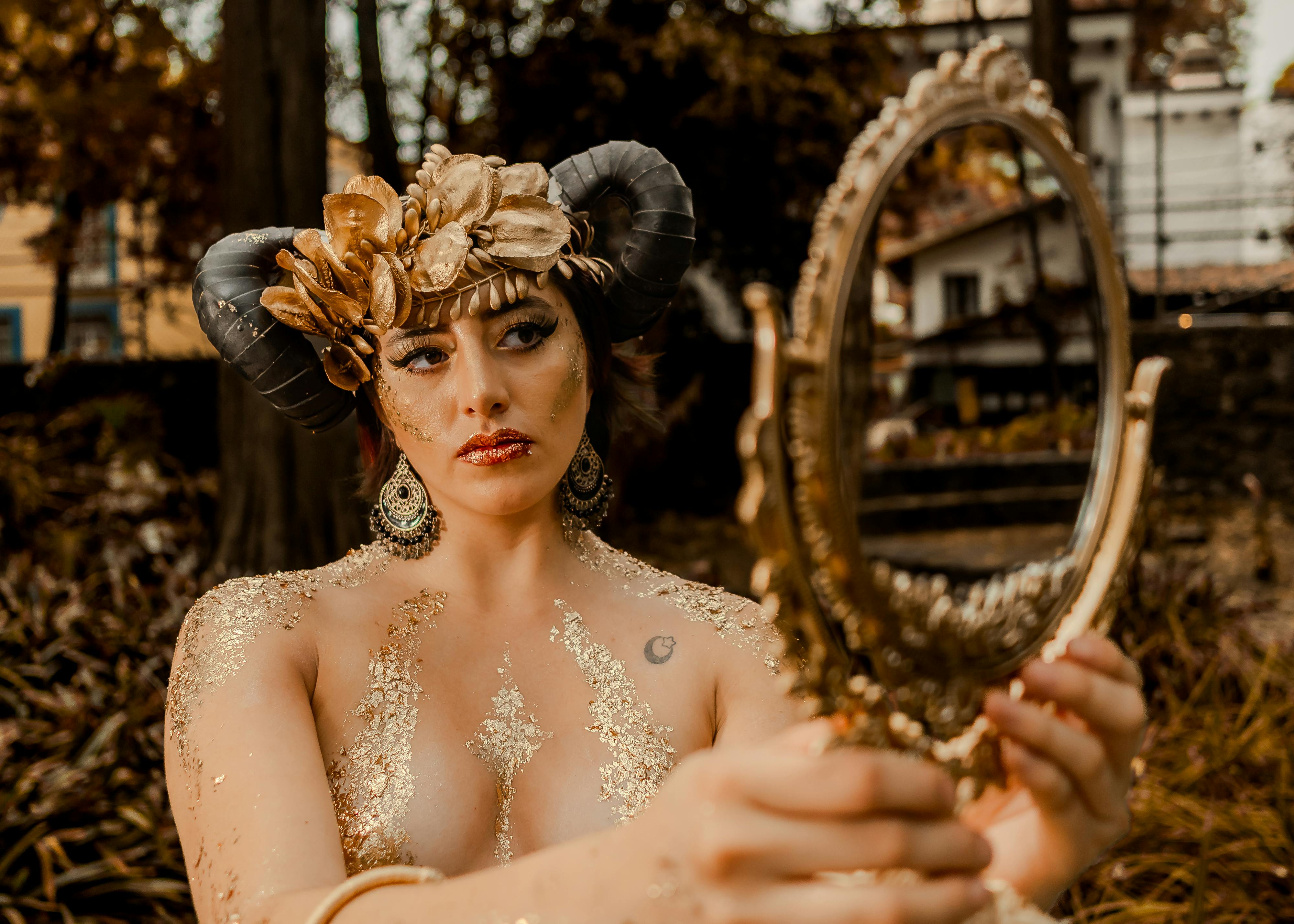 grátis Uma mulher vestida com um traje de fantasia surreal segura um espelho dourado ao ar livre. Foto profissional