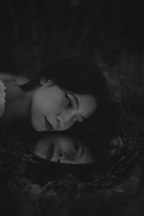 Free Black and white portrait of a woman gazing into a reflective mirror outdoors, creating a surreal mood. Stock Photo