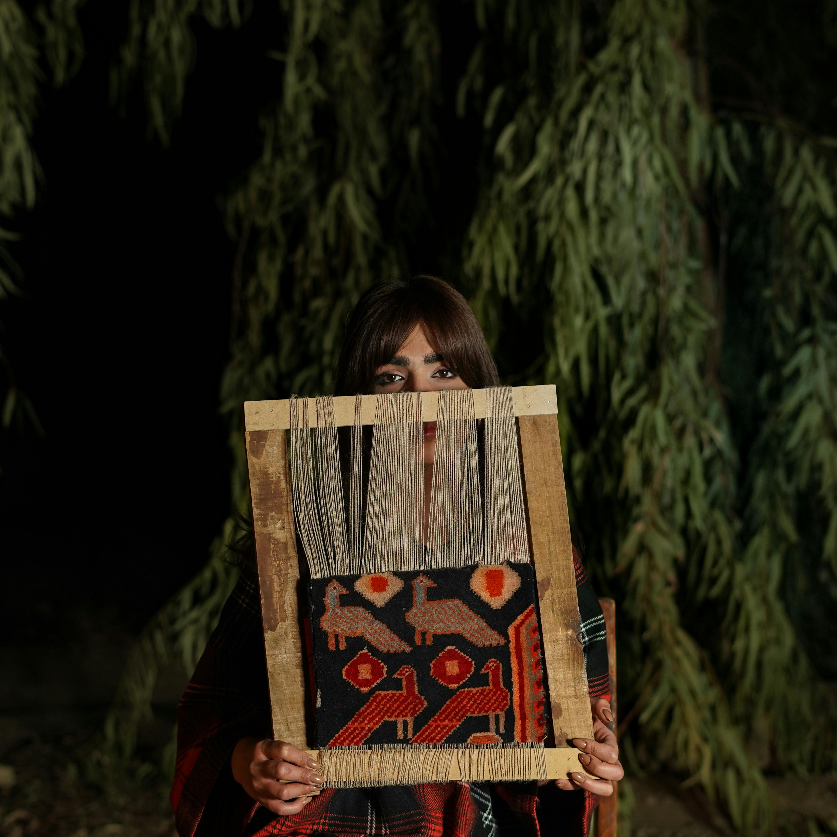 Woman holding a traditional weave frame outdoors under nighttime trees.