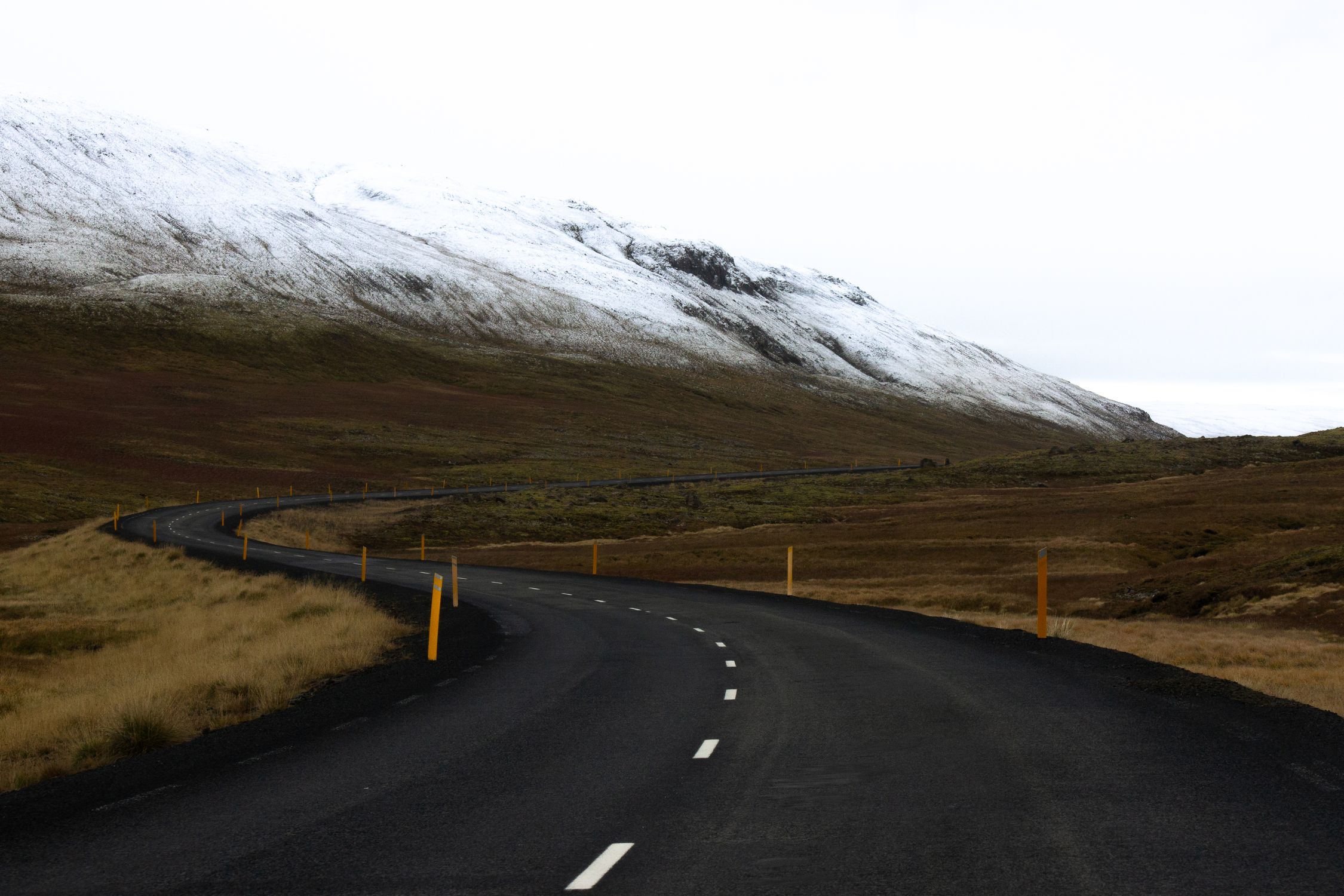 Winding road in Iceland with snow-covered mountains and open landscape, ideal for travel inspiration.