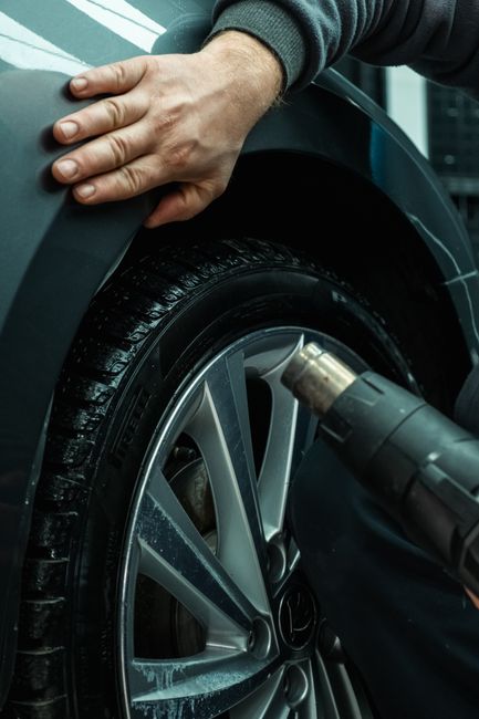 Hands working on a car tire using a heat gun, showing automotive maintenance in a workshop setting.