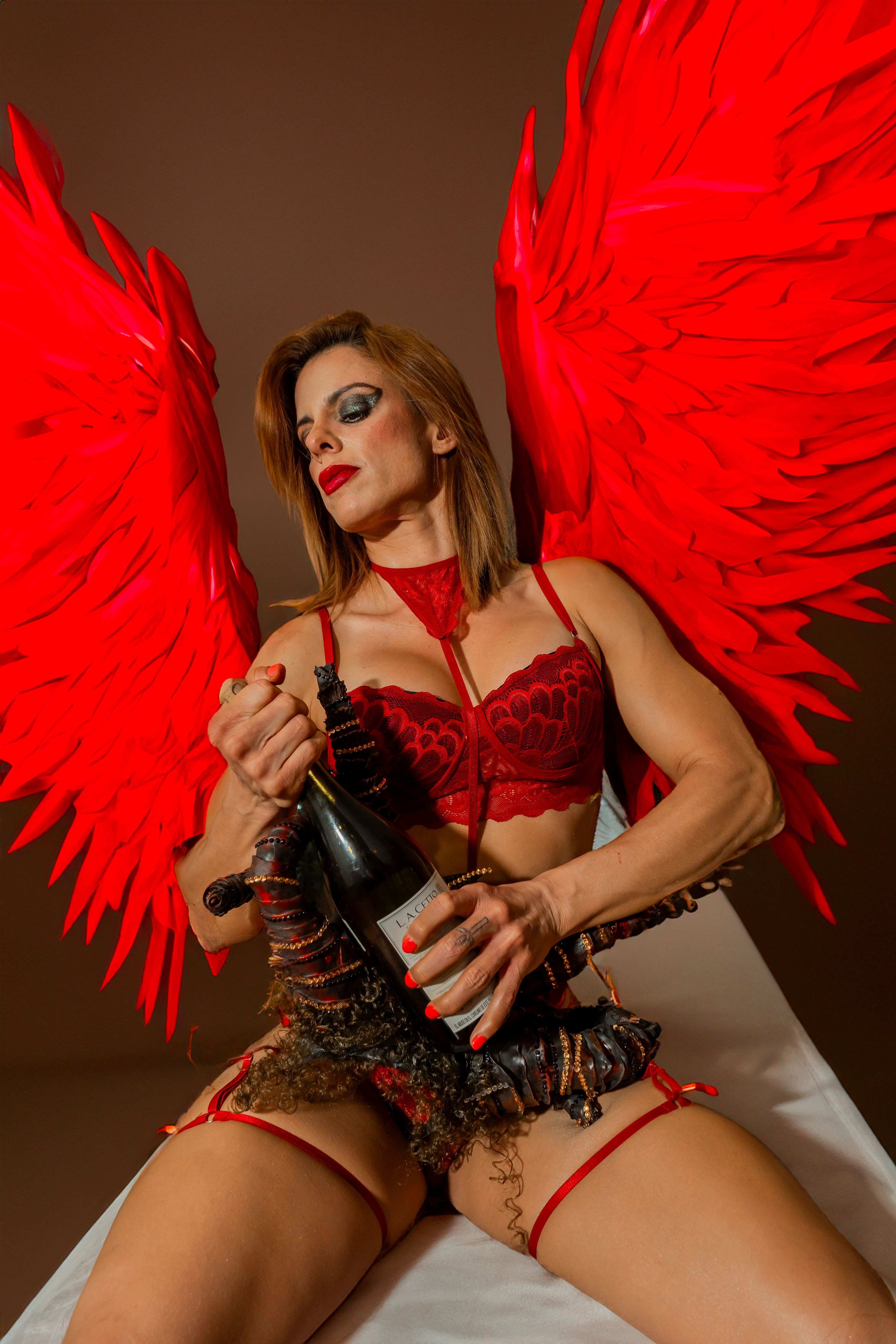A surreal and bold fantasy portrait of a woman with red wings holding a champagne bottle.