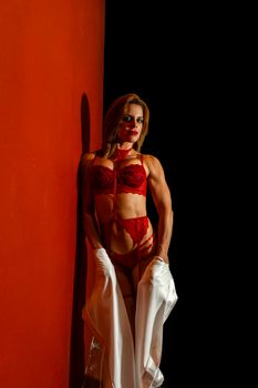 Confident woman in red lingerie poses against a striking red wall with low light ambiance.