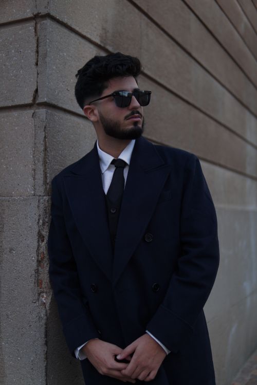 Free A fashionable bearded man poses stylishly in a suit and sunglasses, leaning against an outdoor wall. Stock Photo