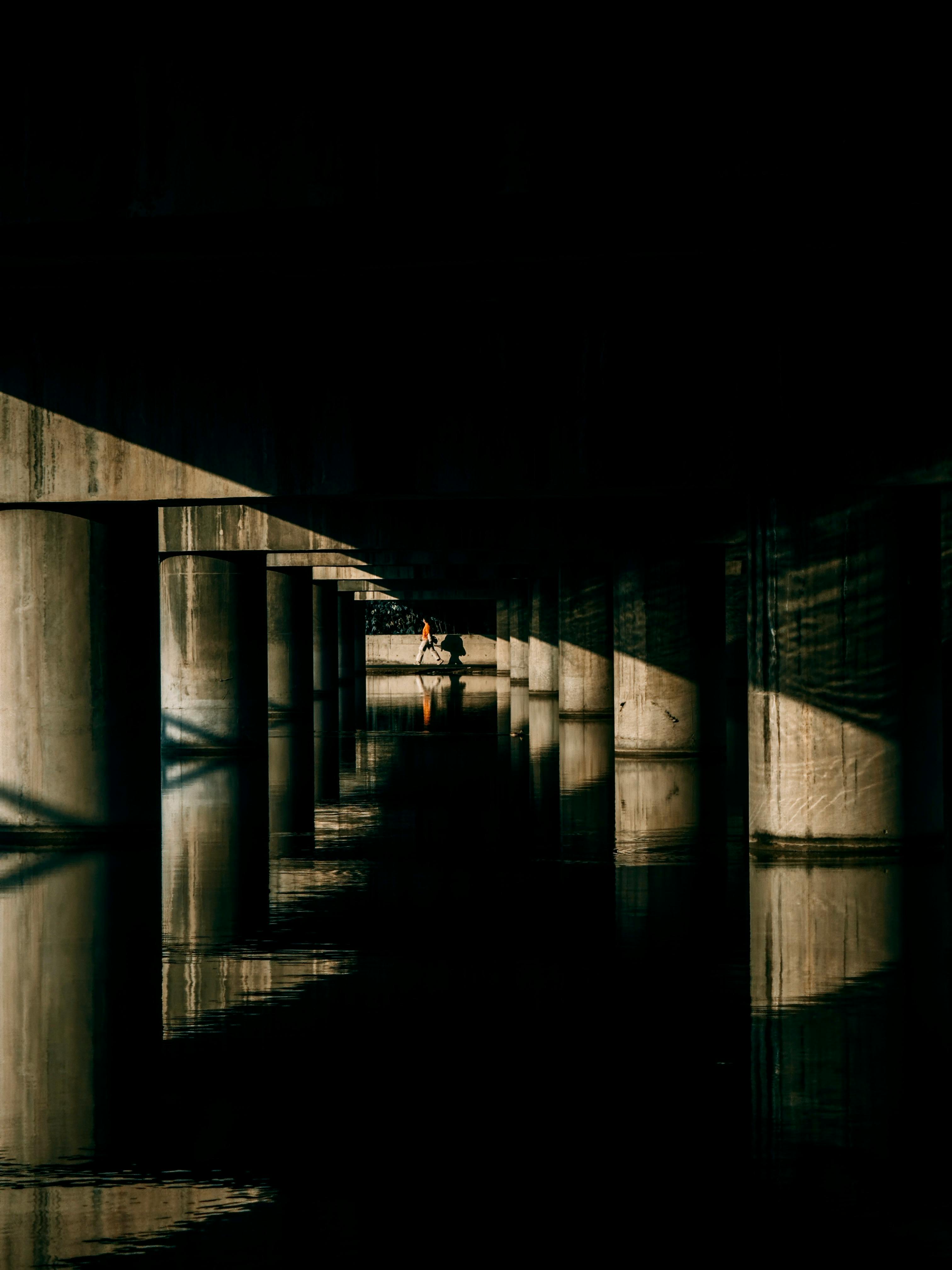 Silhouette of a man under a modern bridge with dramatic shadows and reflections.