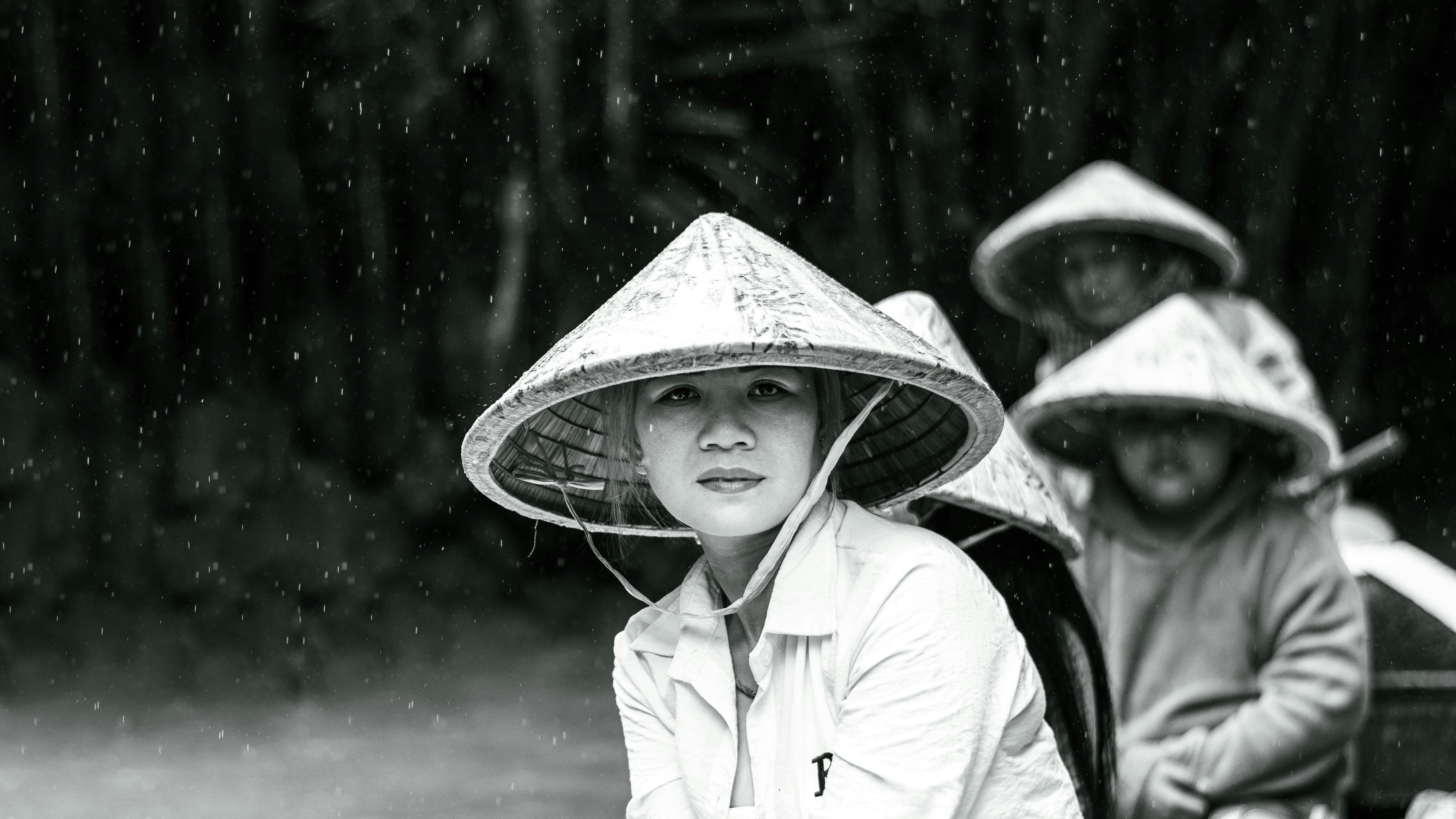 A black and white portrait of Vietnamese locals in traditional hats during rain.