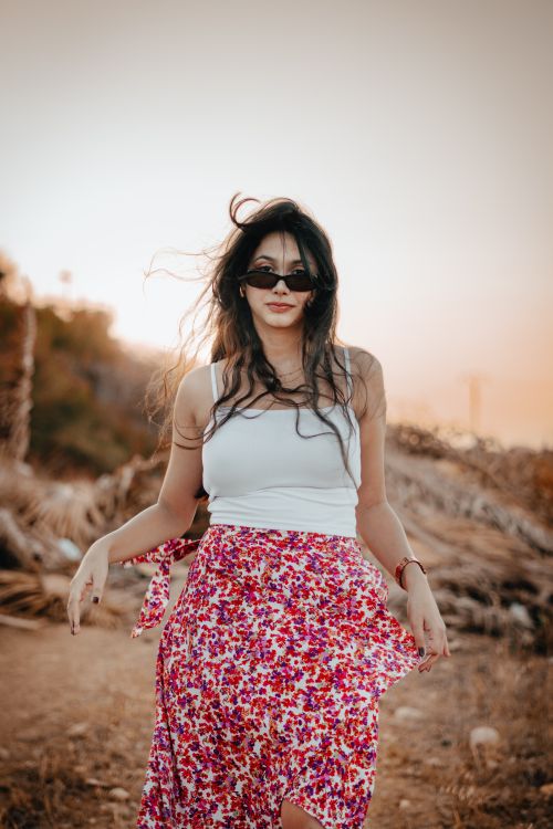 Free Stylish woman in sunglasses and floral skirt enjoying a warm sunset outdoors. Stock Photo