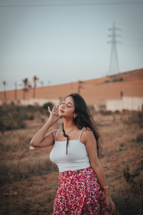 Free Woman standing in a field, enjoying a peaceful moment at sunset, with power lines in the background. Stock Photo