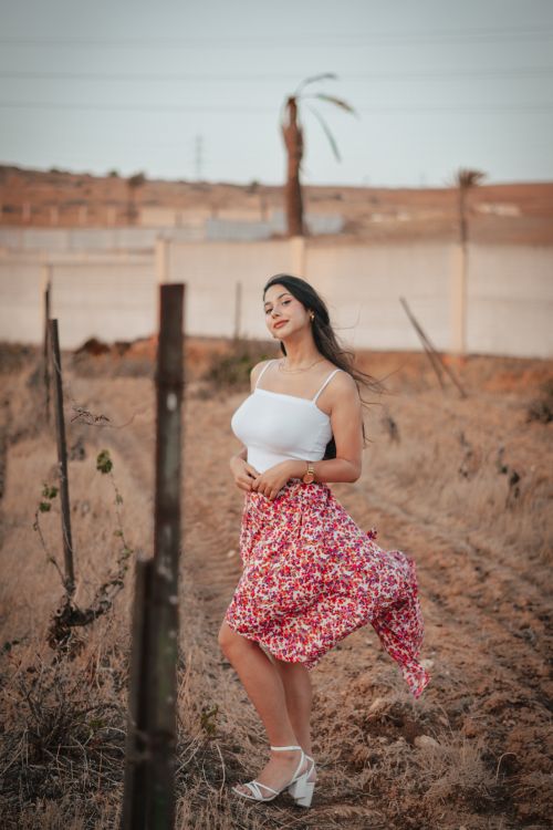Free A serene portrait of a young woman in a vibrant floral skirt, standing in a dry rural setting with a gentle breeze. Stock Photo