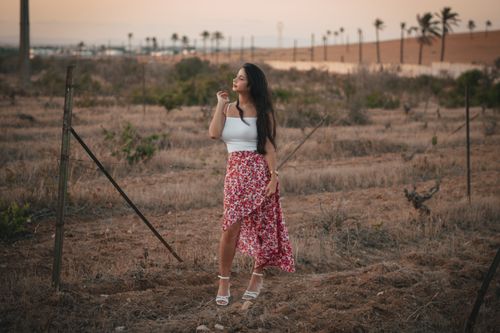 Free Woman standing outdoors in floral skirt enjoying nature's beauty at sunset. Stock Photo