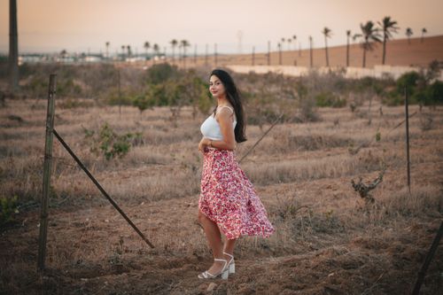 Free A young woman in a floral skirt poses in a sunlit rural landscape with palm trees. Stock Photo