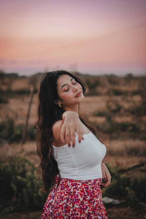 Free A young woman stands peacefully in a floral skirt during a summer sunset, basking in the tranquil surroundings. Stock Photo