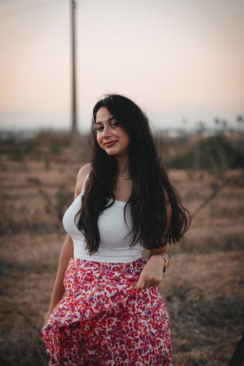 Free A woman smiling in a field, wearing a white top and floral skirt during sunset. Stock Photo