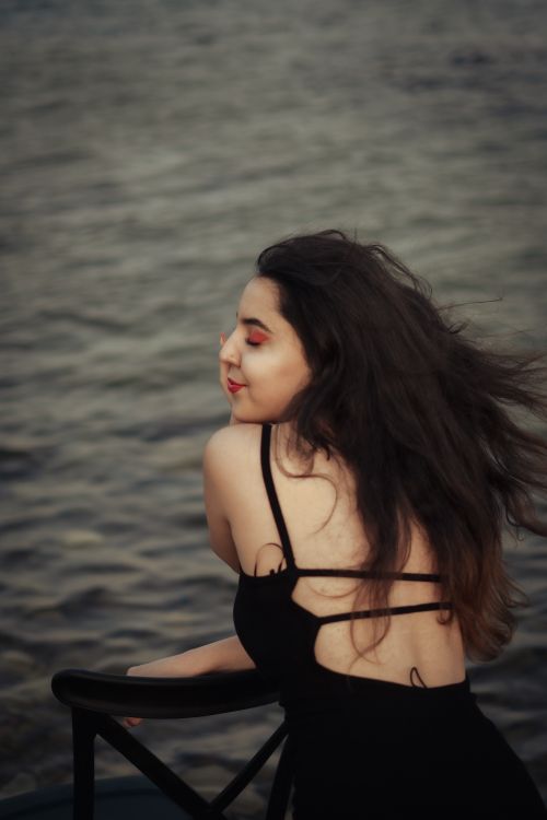 Free A woman in a black dress poses gracefully by the water, showcasing elegance and style. Stock Photo