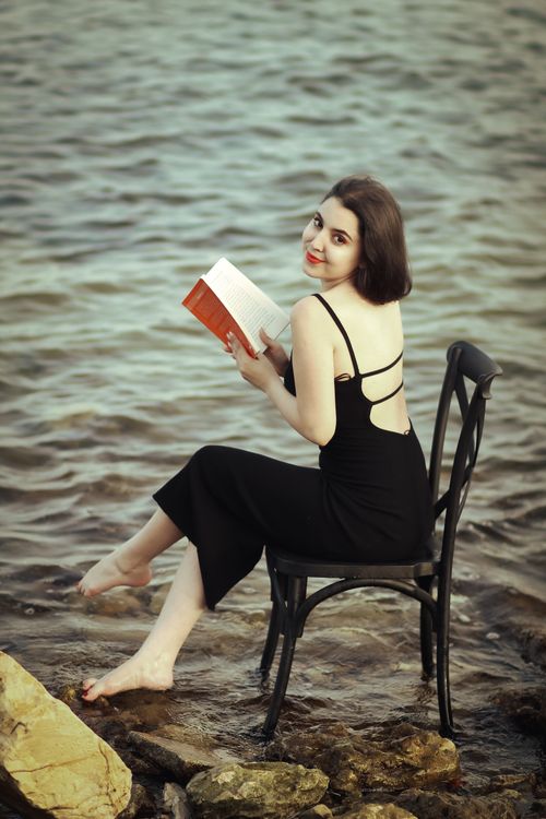 Free Elegantly dressed woman reading by the water's edge, a serene moment. Stock Photo