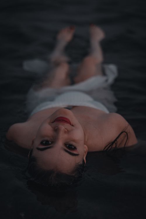 Free A serene woman floats in calm dark water, exuding a peaceful and mysterious aura. Stock Photo