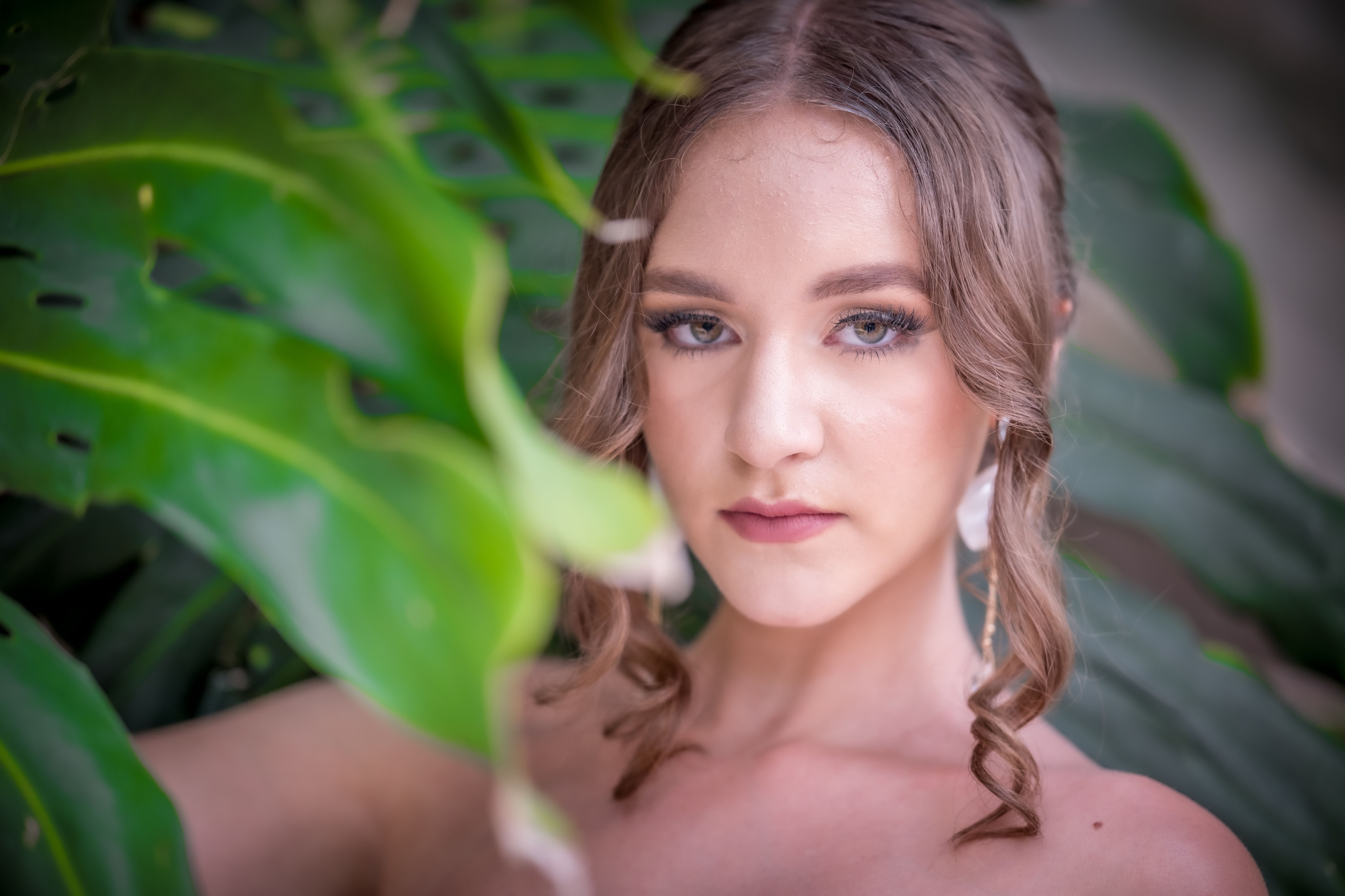 Portrait of a woman in nature with Monstera leaves, showcasing natural beauty.