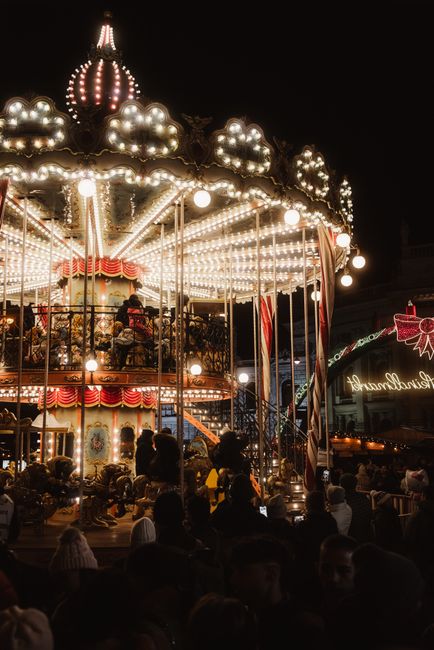 A vibrant carousel illuminated at night, surrounded by a joyful crowd in a festive atmosphere.