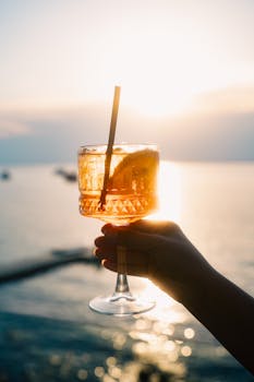 A vibrant cocktail held against a stunning Antalya sunset, capturing the essence of a perfect summer evening.