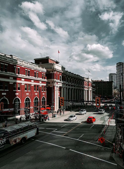 Free Street view of an urban cityscape featuring historical architecture and bustling traffic under a cloudy sky. Stock Photo