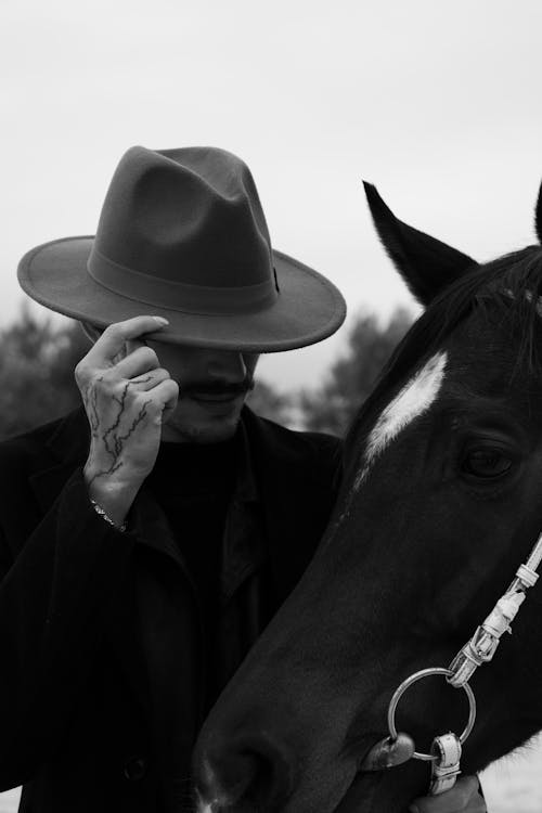 Free A man in a hat with a horse in a black and white photo, exuding a mysterious vibe. Stock Photo