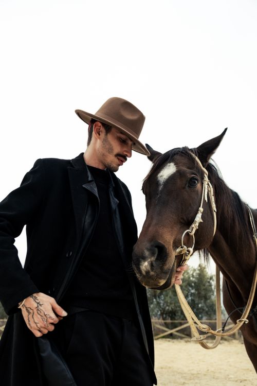 Free A stylish man in a cowboy hat stands closely with a horse in an outdoor setting. Stock Photo