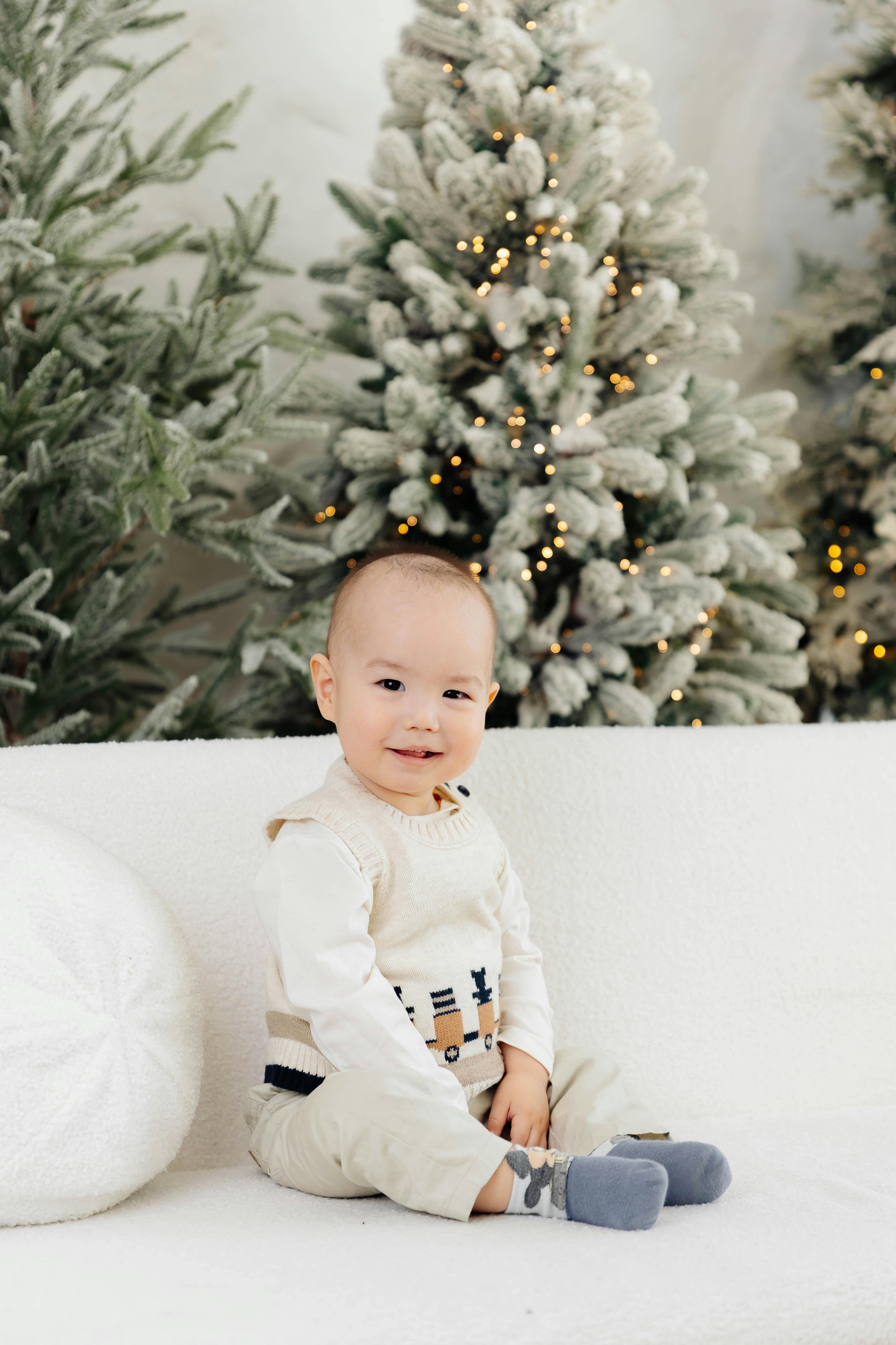 Cute baby sitting in a cozy setting with decorated Christmas trees.