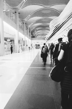 Monochrome view of travelers walking through İstanbul Airport, Türkiye. Dynamic composition.