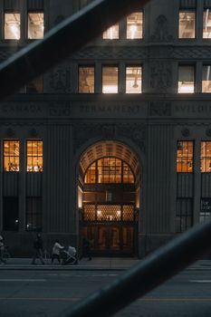 Nighttime urban scene of the Canada Permanent Building in Toronto with pedestrians on the street.