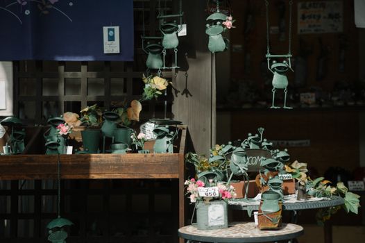 Collection of whimsical frog figurines in a Japanese shop adorned with flowers and priced signs.
