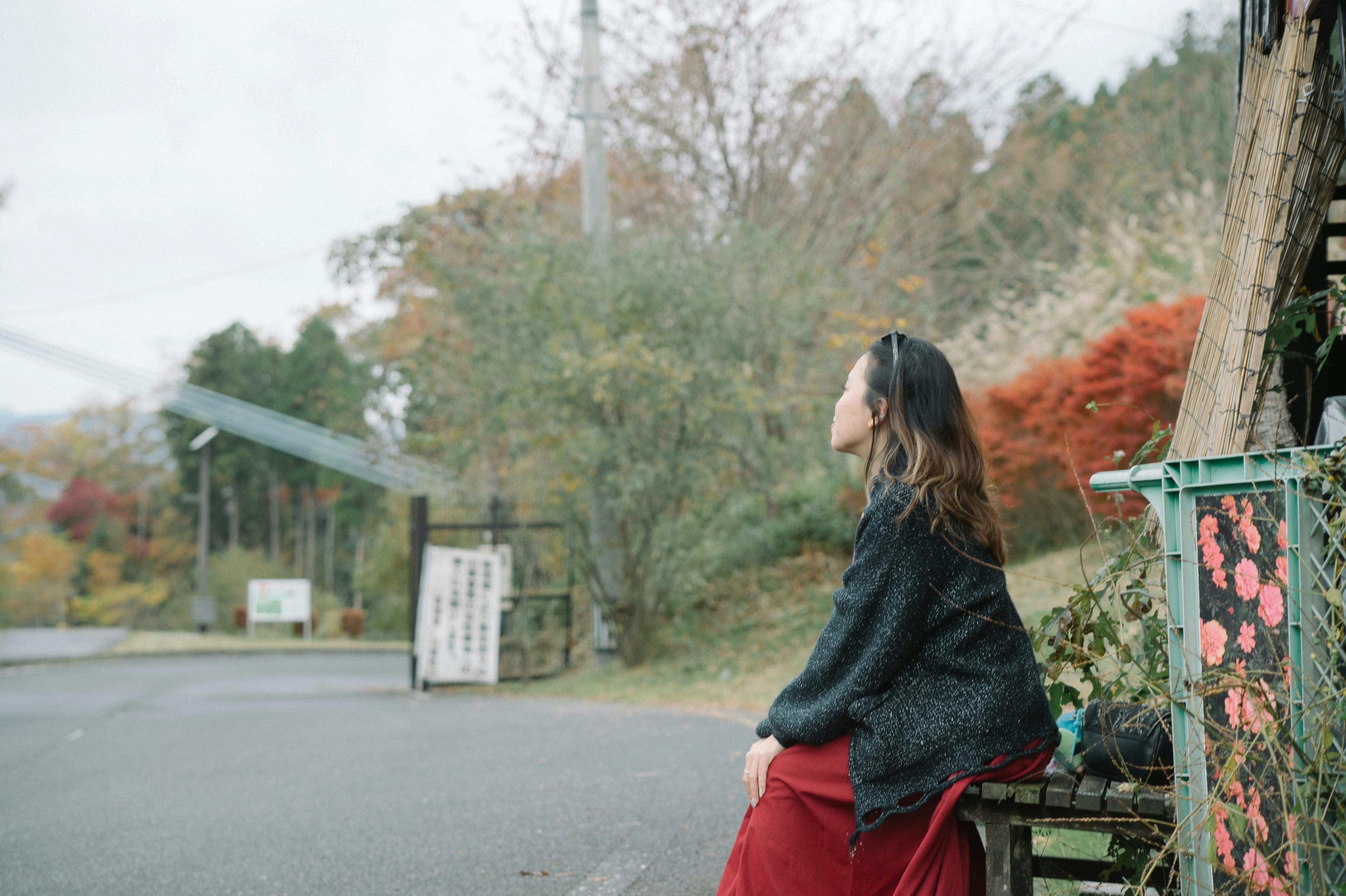 A woman seated outside in a serene Japanese rural landscape during autumn.
