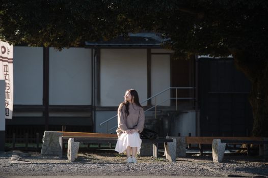 A young woman enjoying a sunny day on a bench under a tree in Japan.