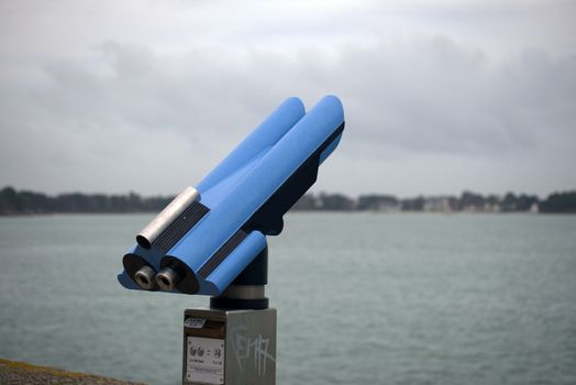 A blue public telescope facing the ocean, ideal for scenic viewing and tourism.