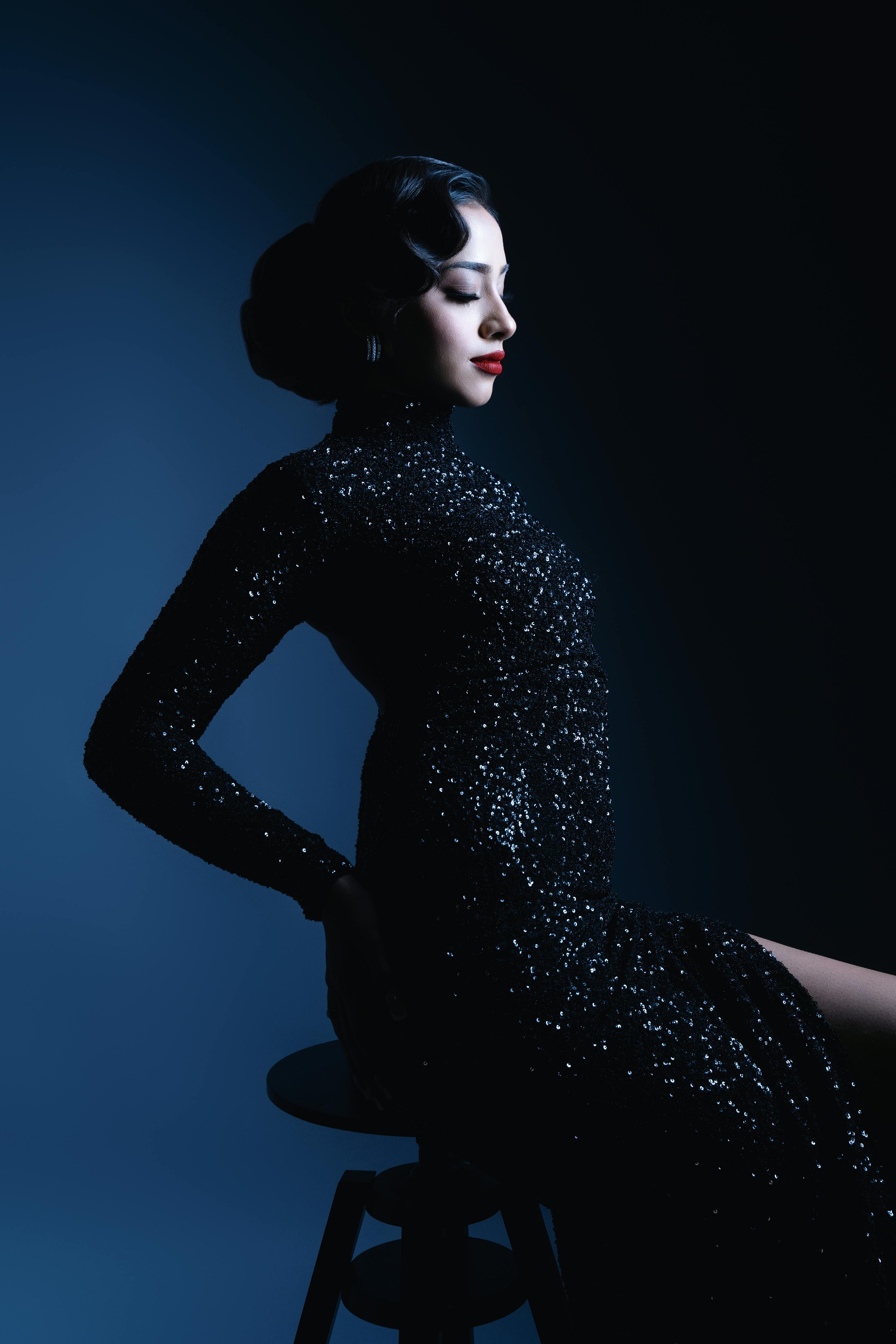 Bezpłatne Artystyczny portret kobiety w lśniącej czarnej sukience wykonany w efektownym oświetleniu studyjnym. Zdjęcie z galerii