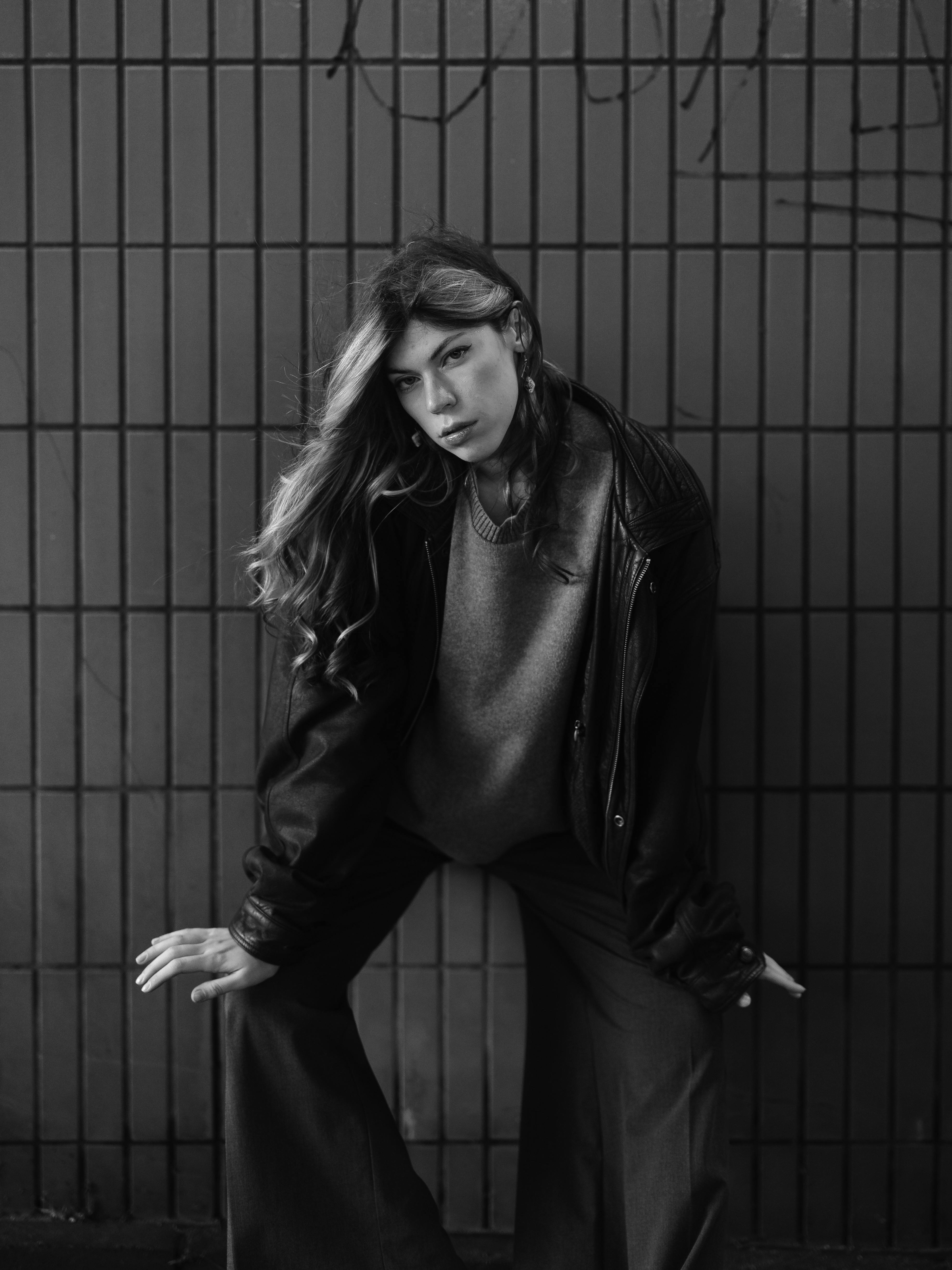 Moody black and white portrait of a stylish young adult posing against a metal fence.