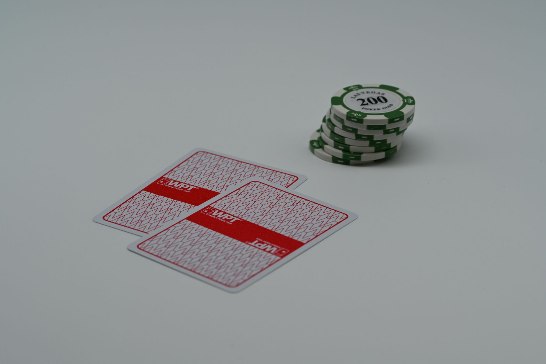 Close-up of poker playing cards and green chips on a white background, highlighting the simplicity of a gaming scene.