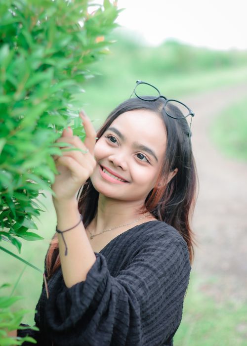 Free Young woman smiling and touching leaves while enjoying a walk in nature. Stock Photo