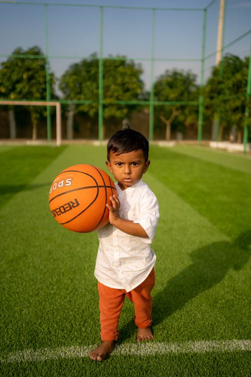 Free A young child playing with a basketball on a green turf field under clear skies in Chittagong, Bangladesh. Stock Photo