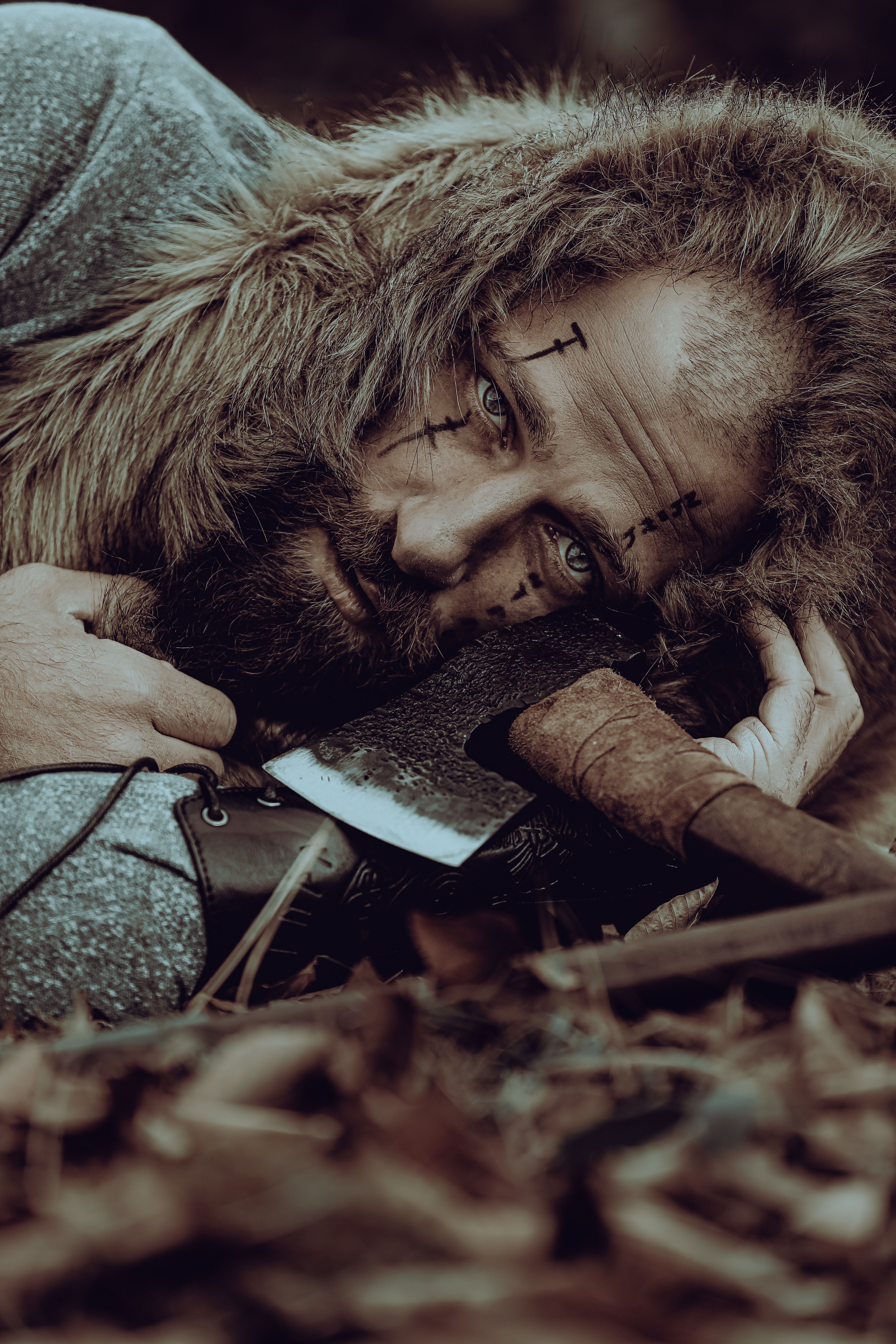 A bearded medieval warrior in costume rests outdoors, holding a battle axe.