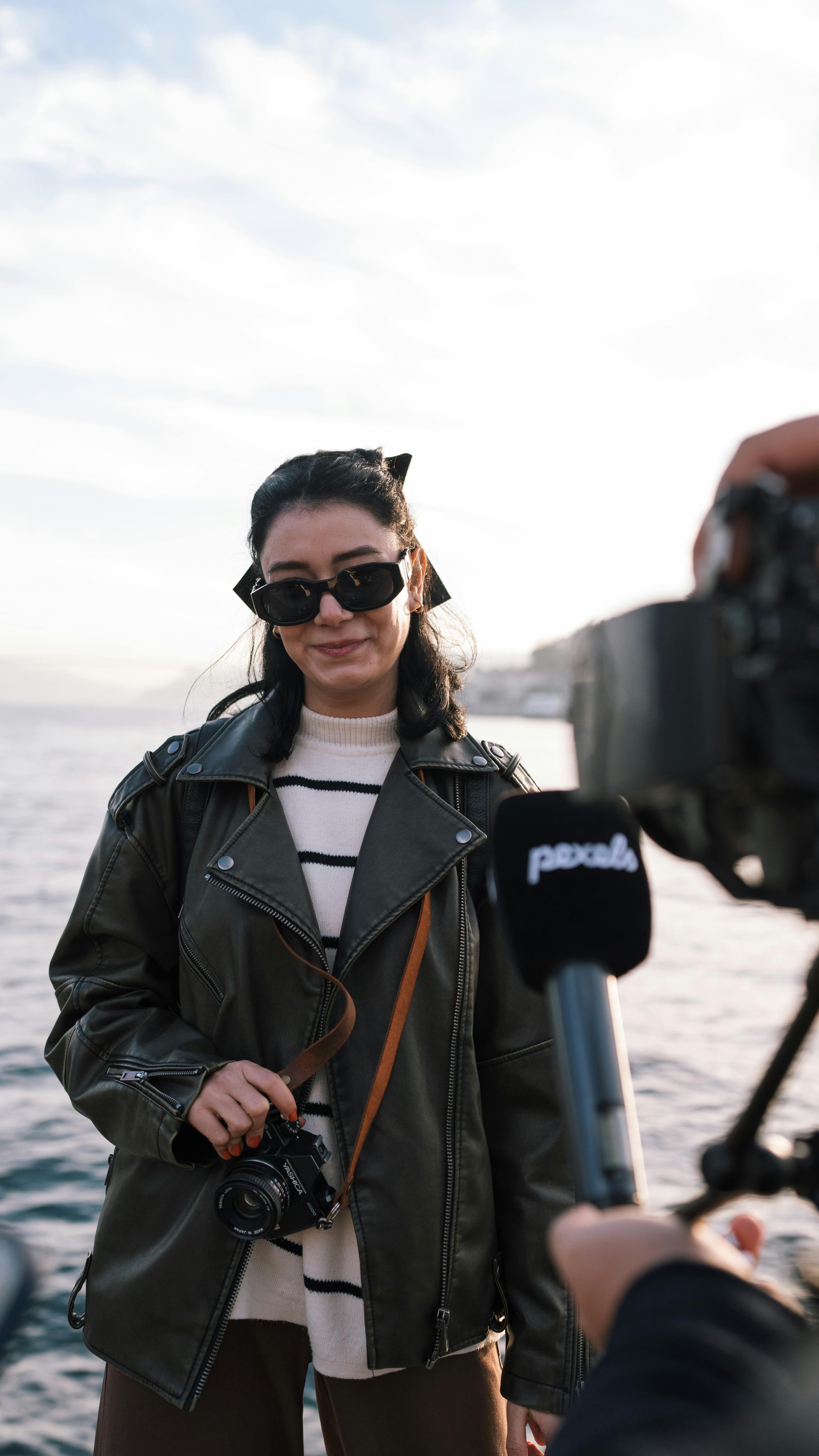Smiling woman in sunglasses by the sea being interviewed. Captured candid moment.