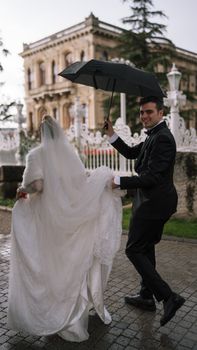 Bride and groom joyfully walk in the rain sharing an umbrella at an elegant venue.