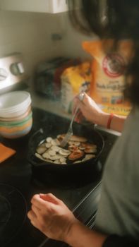 Person cooking sliced potatoes in a frying pan on a home kitchen stovetop.