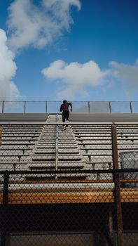 A man exercises by running up stadium bleachers under a bright blue sky.