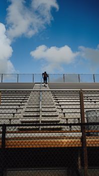 Person stands alone on outdoor bleachers against a vibrant blue sky backdrop.