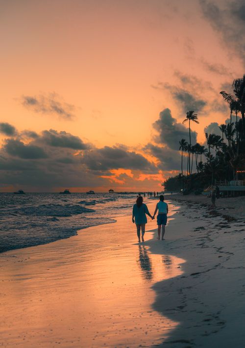 Free Couple walking hand-in-hand along a tropical beach at sunset, creating a romantic ambiance. Stock Photo