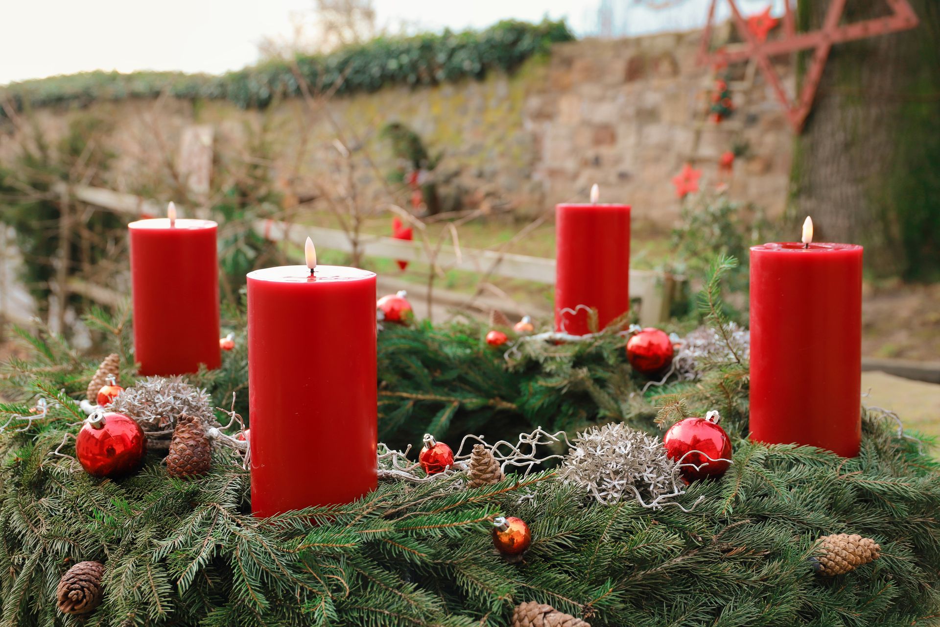 A vibrant outdoor advent wreath with four red candles and pine decorations.