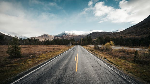 A picturesque road stretches towards snowy mountains under a bright sky, capturing natural beauty and serenity.