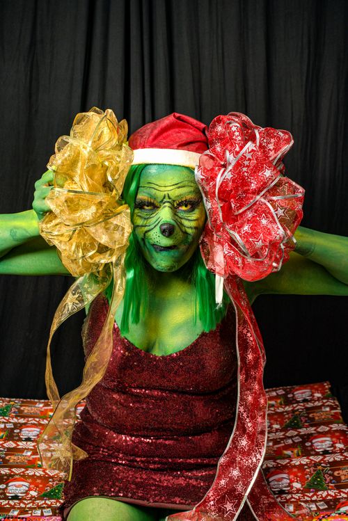 Free Person in Grinch costume with festive holiday bows on Christmas-themed backdrop. Stock Photo