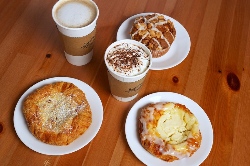 Flat lay of assorted breakfast pastries and coffee cups on a wooden table.