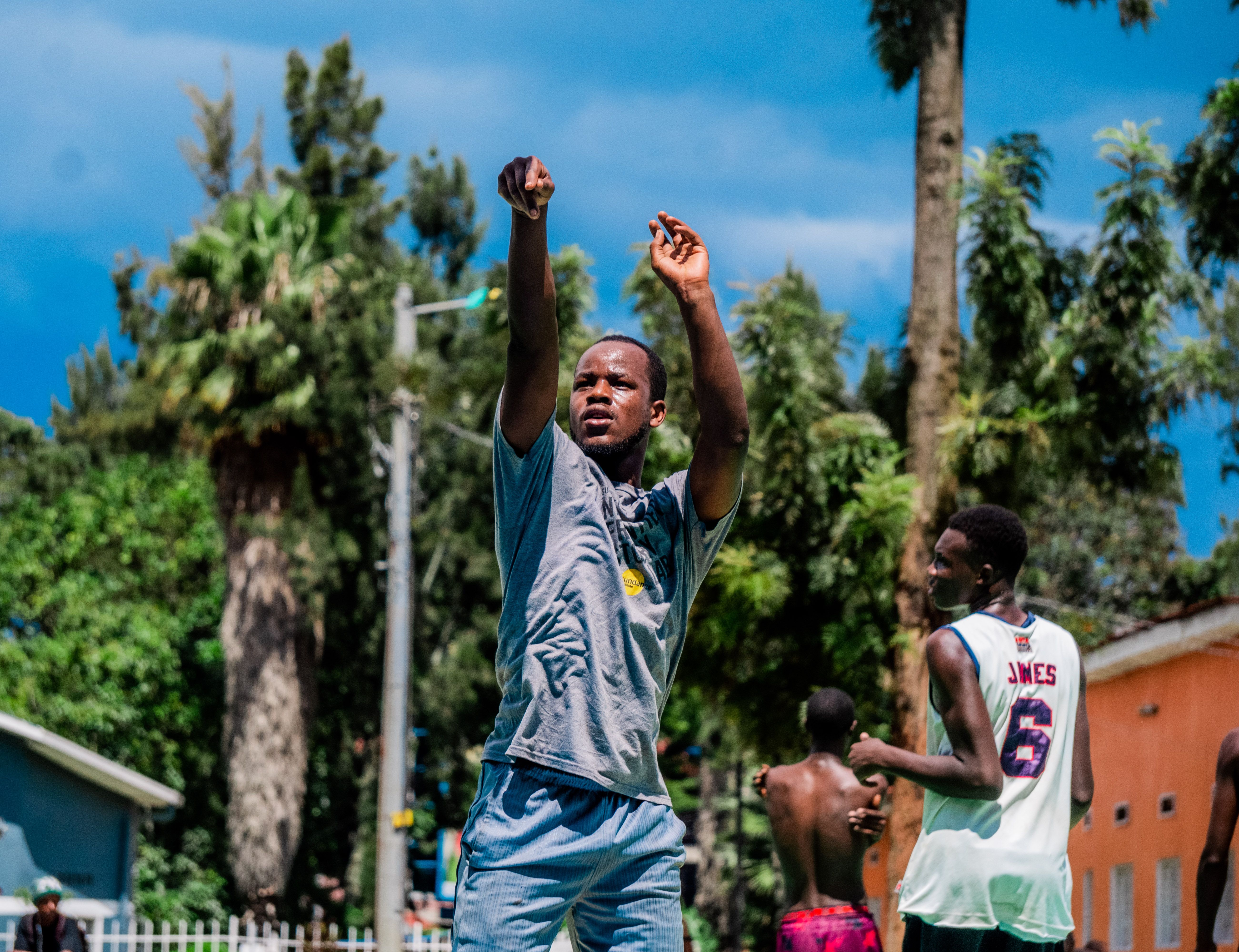 Young adults playing basketball outdoors on a sunny day with lush green trees.